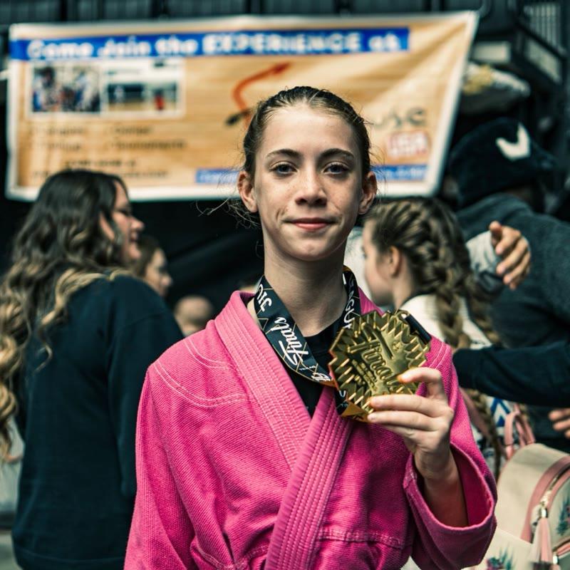 Young athlete in pink gi with JJWL Finals gold medal