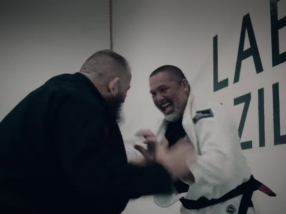 Two adults in gis laugh as they grip up at Labyrinth BJJ in Fulshear, TX
